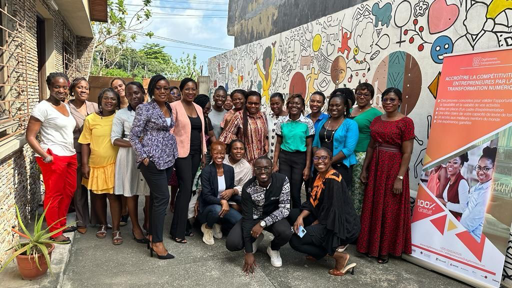 Group of women entrepreneurs gathered beside a program banner and mural.
