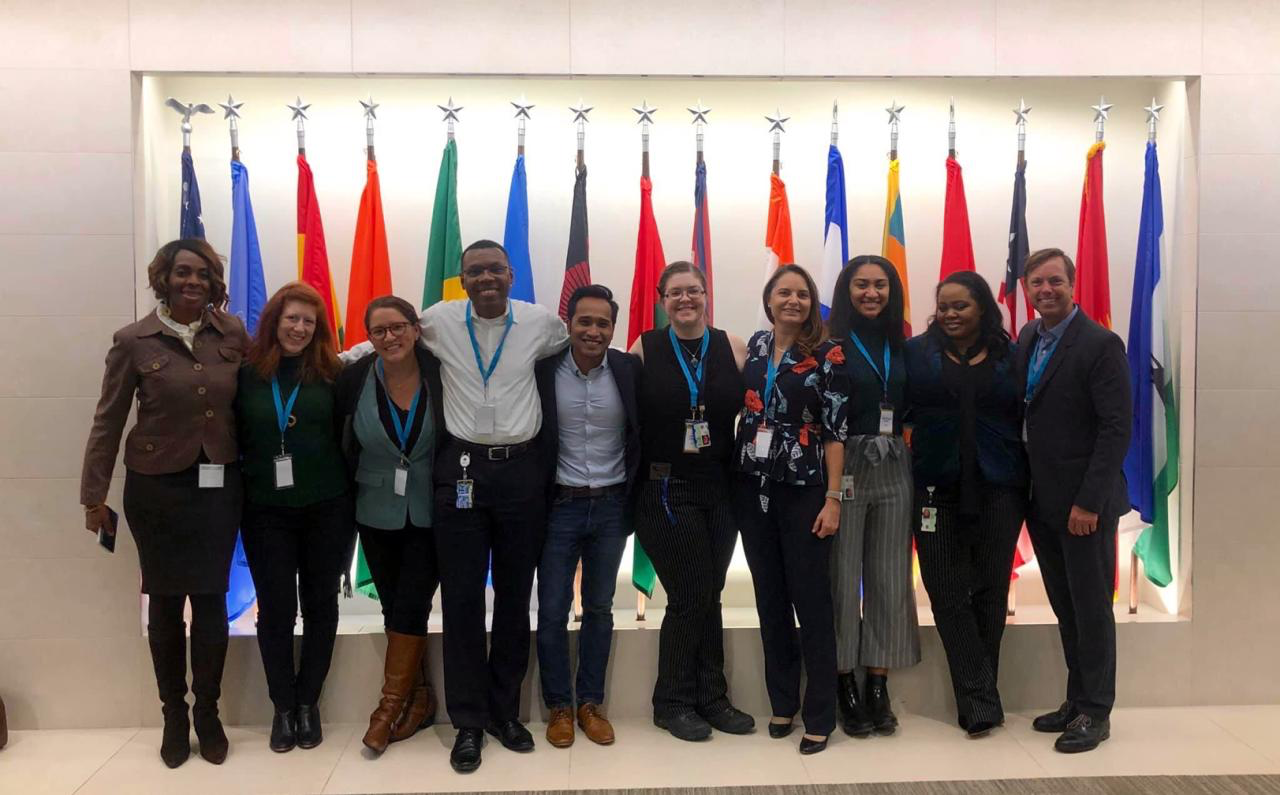 Team standing together in front of a row of international flags.