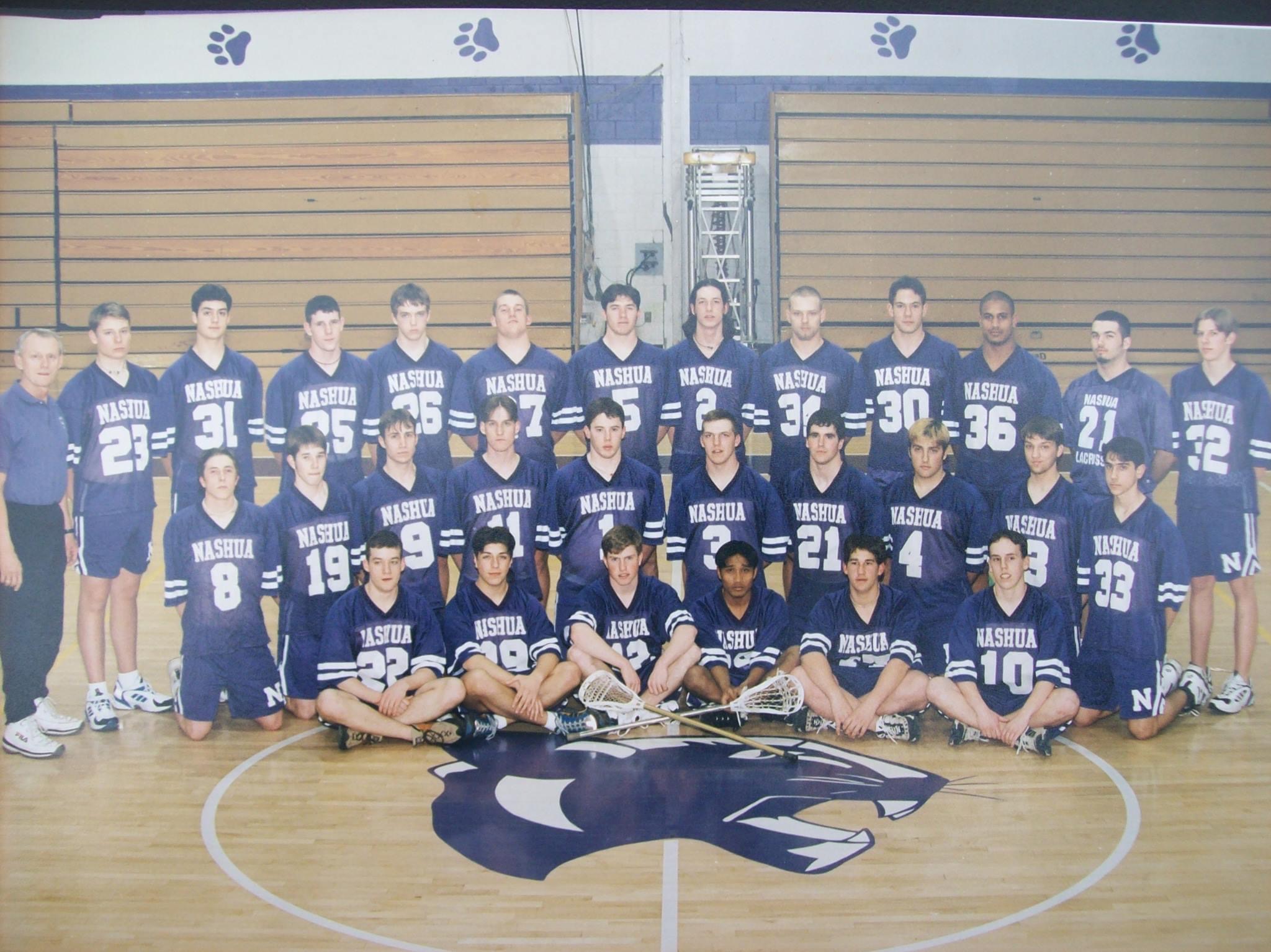 Nashua high school lacrosse team posing together in a gymnasium.