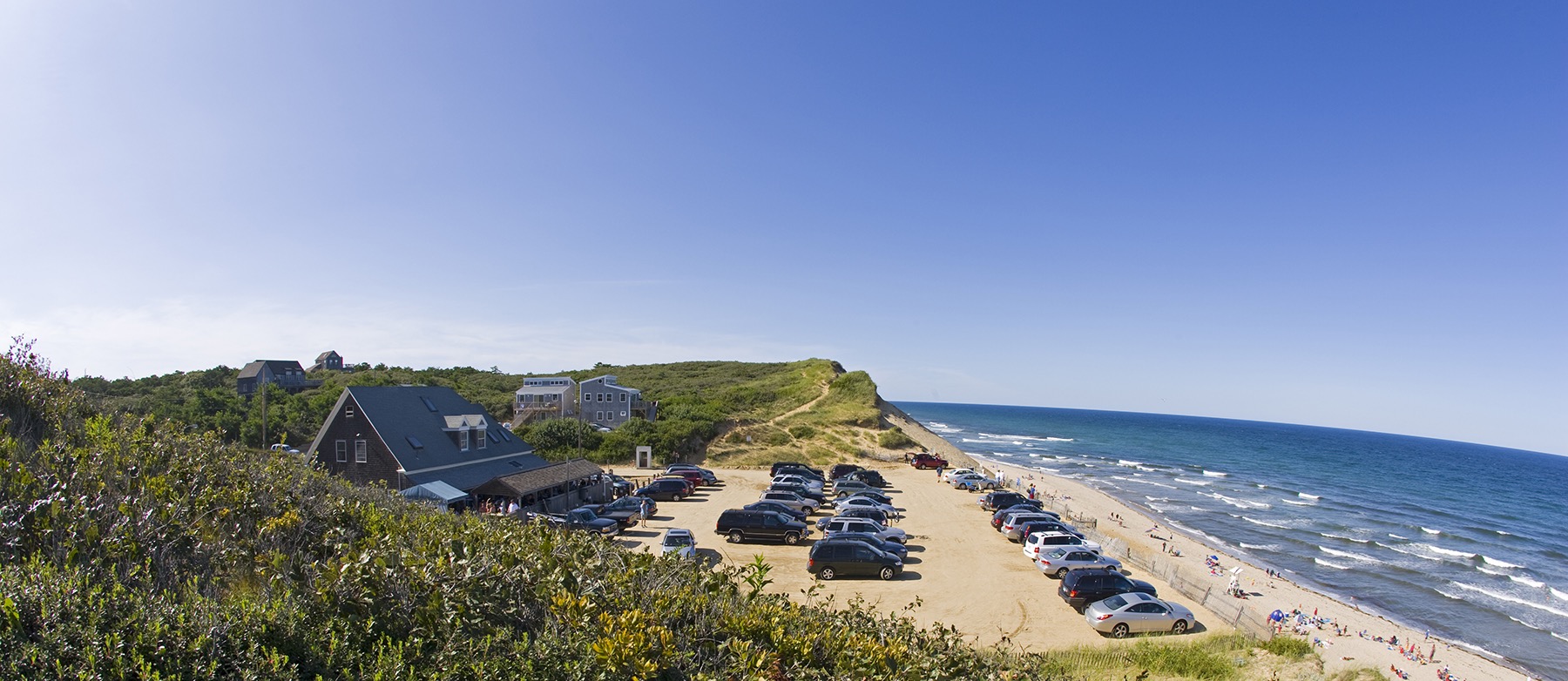 Wide view of a New England coastline with beach, dunes, houses, and the ocean.