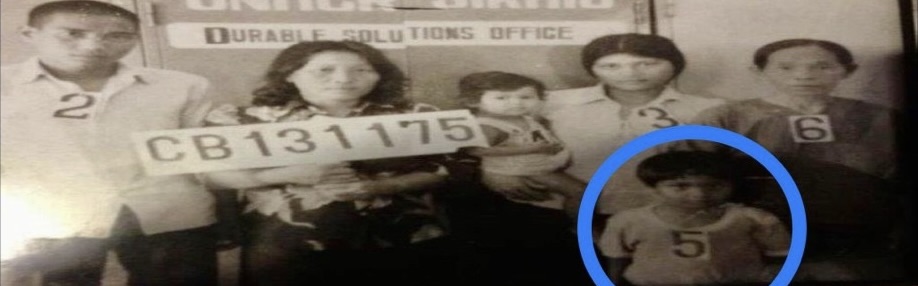 Historic family registration photograph at a refugee camp, with family members wearing numbered identification tags and a blue circle highlighting one child.