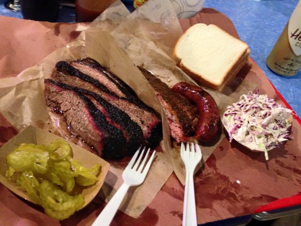 Plate of Texas barbecue with brisket, sausage, pickles, bread, and coleslaw.