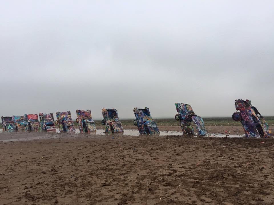 Painted cars partially buried in the ground at Cadillac Ranch beneath an overcast sky.