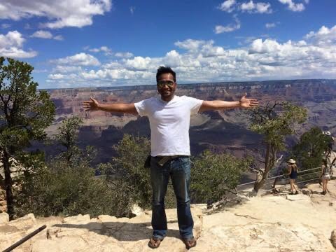 Person standing with arms outstretched in front of the Grand Canyon.