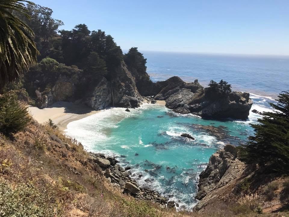 Rocky California coastal cove with turquoise water and ocean beyond.