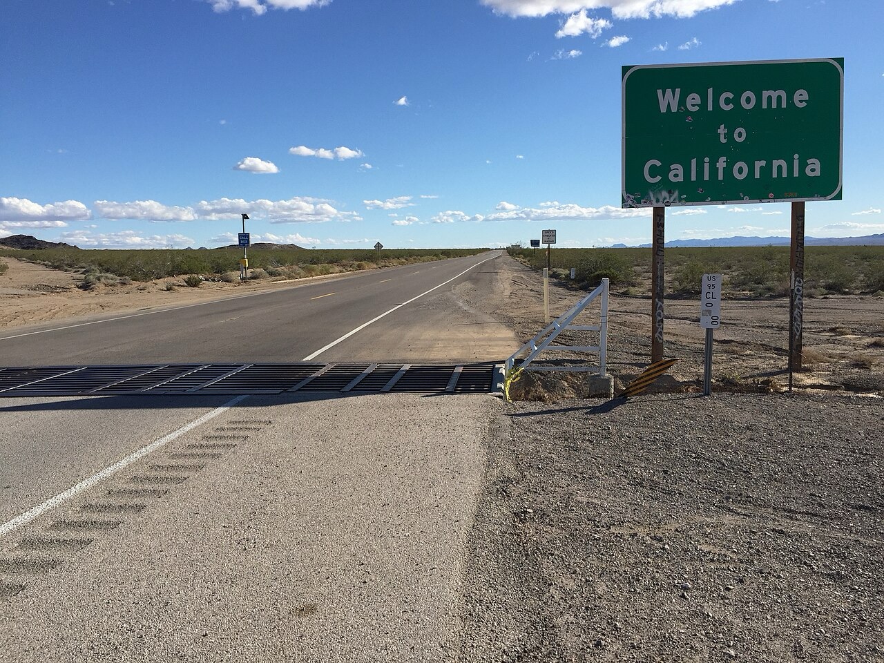 Welcome to California highway sign beside a desert road.