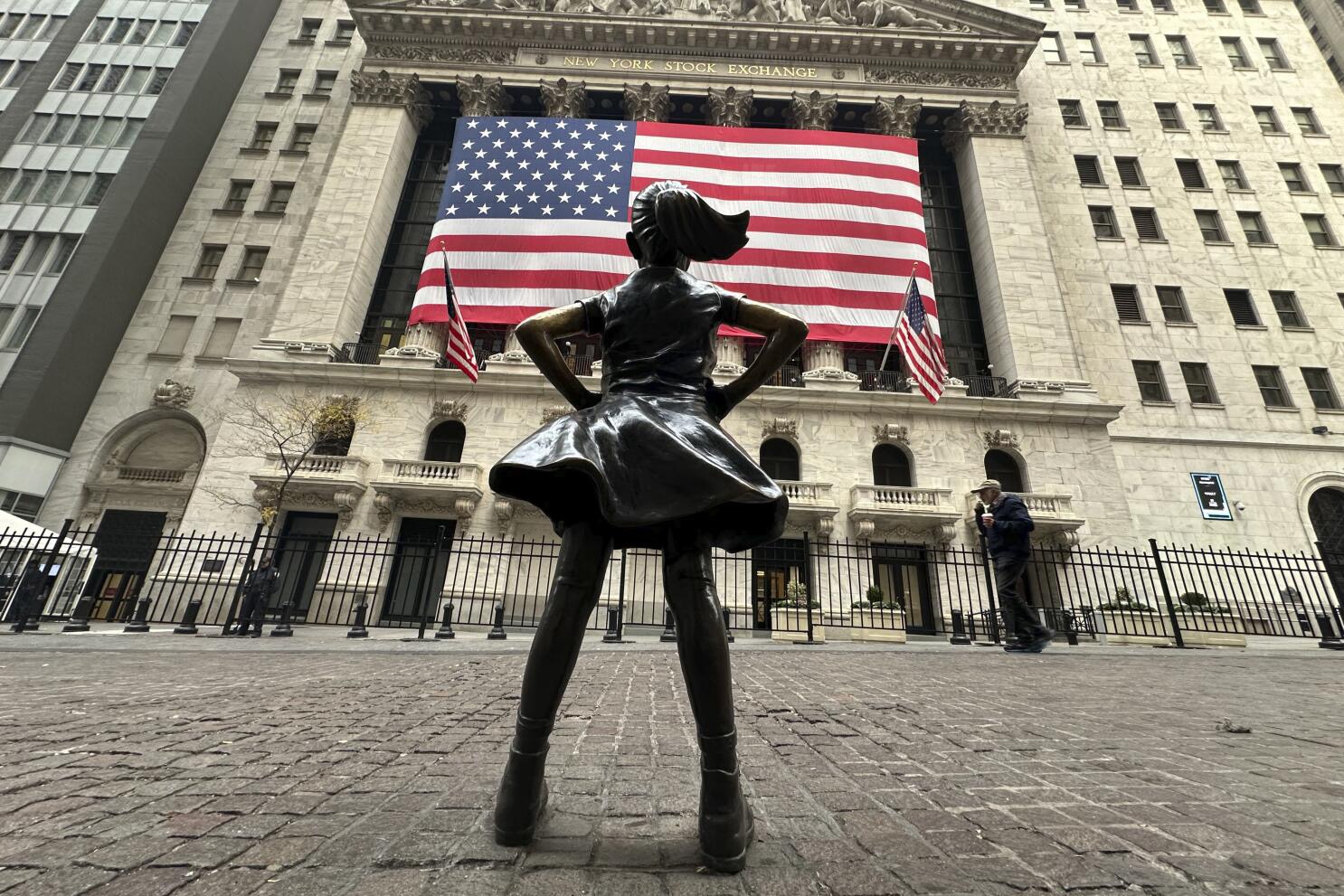 Fearless Girl statue standing in front of the New York Stock Exchange beneath a large American flag.