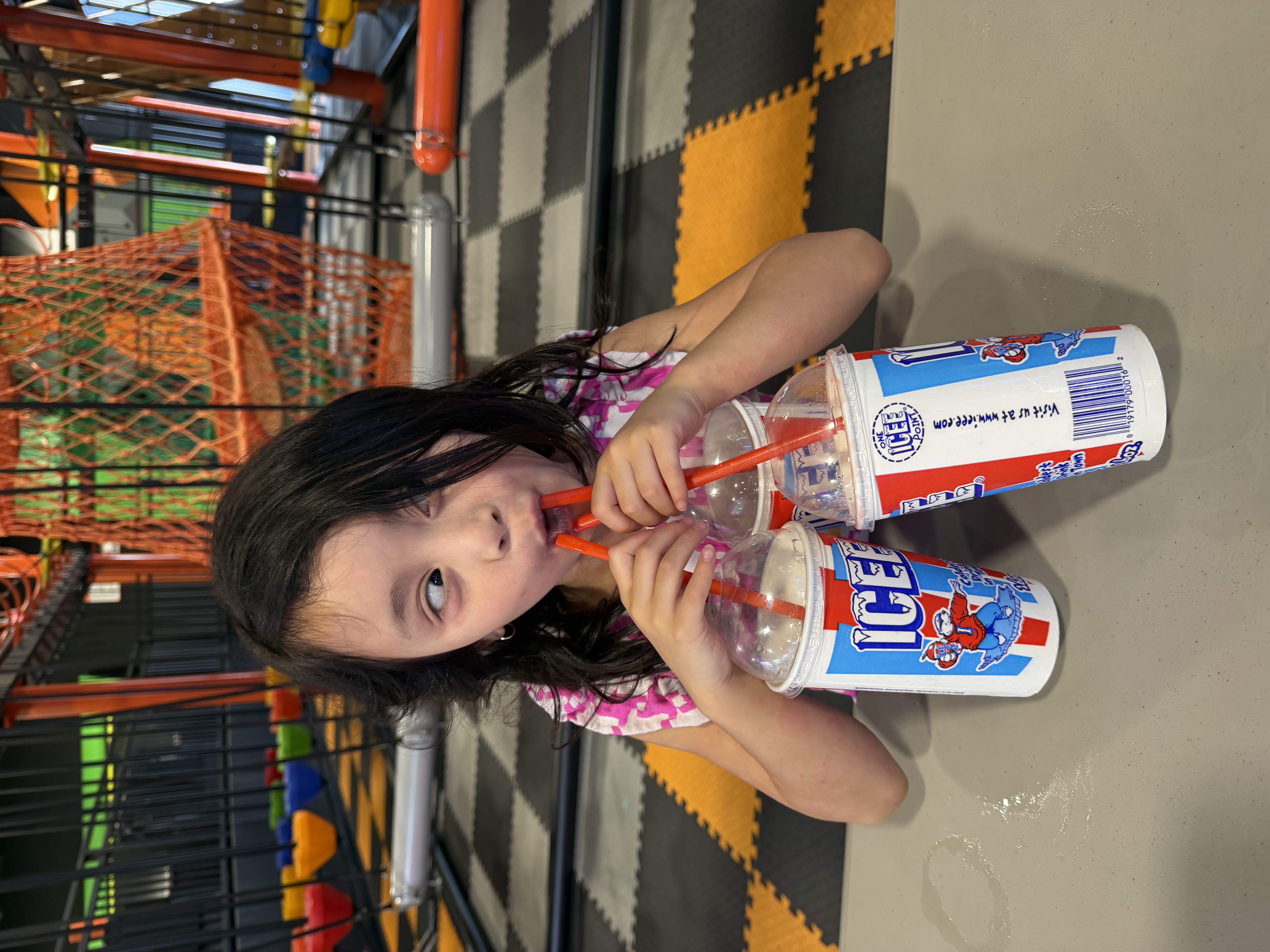A child playfully drinking from several frozen drinks at once.