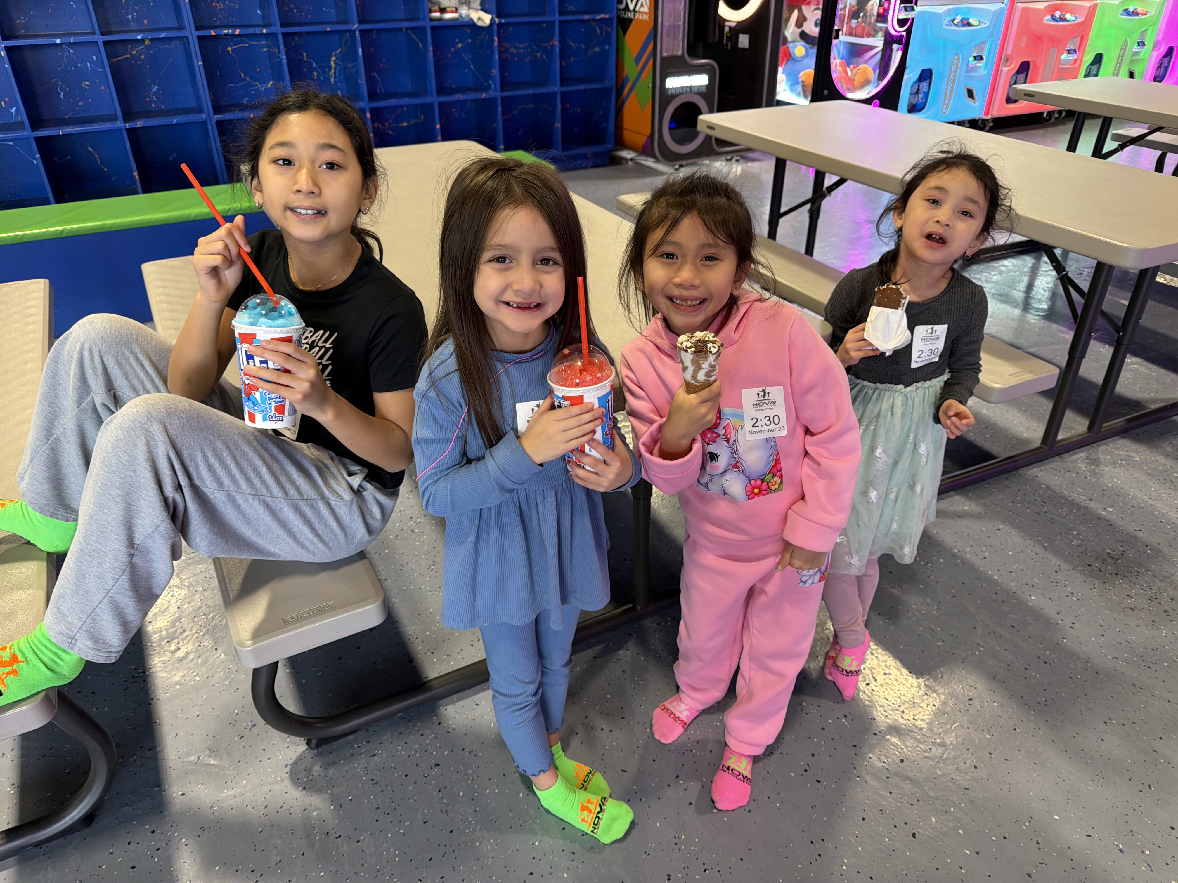 Four children smiling together with frozen drinks and ice cream at an indoor activity center.