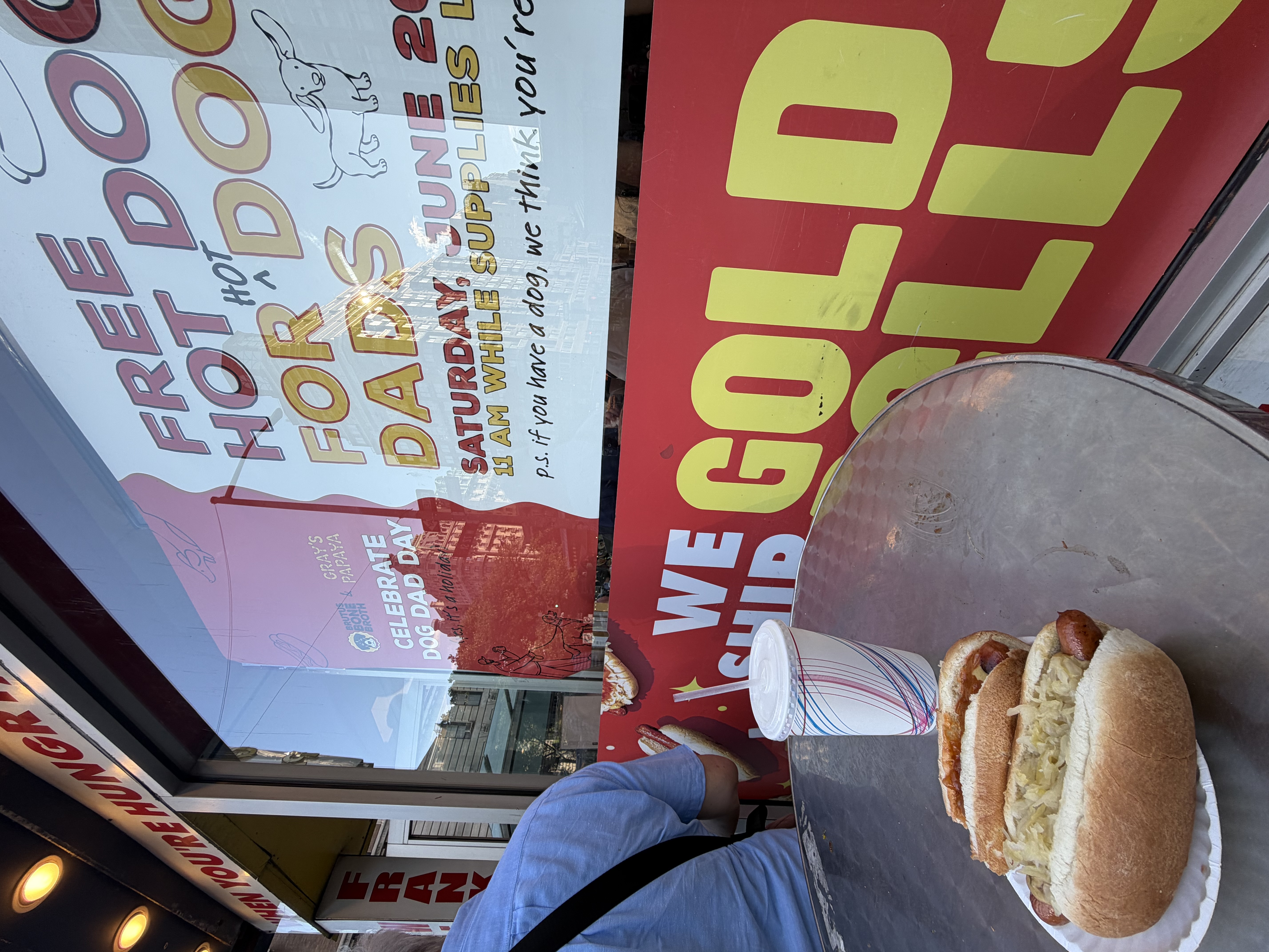 Hot dogs and a drink from Gray’s Papaya beside a promotional window sign.