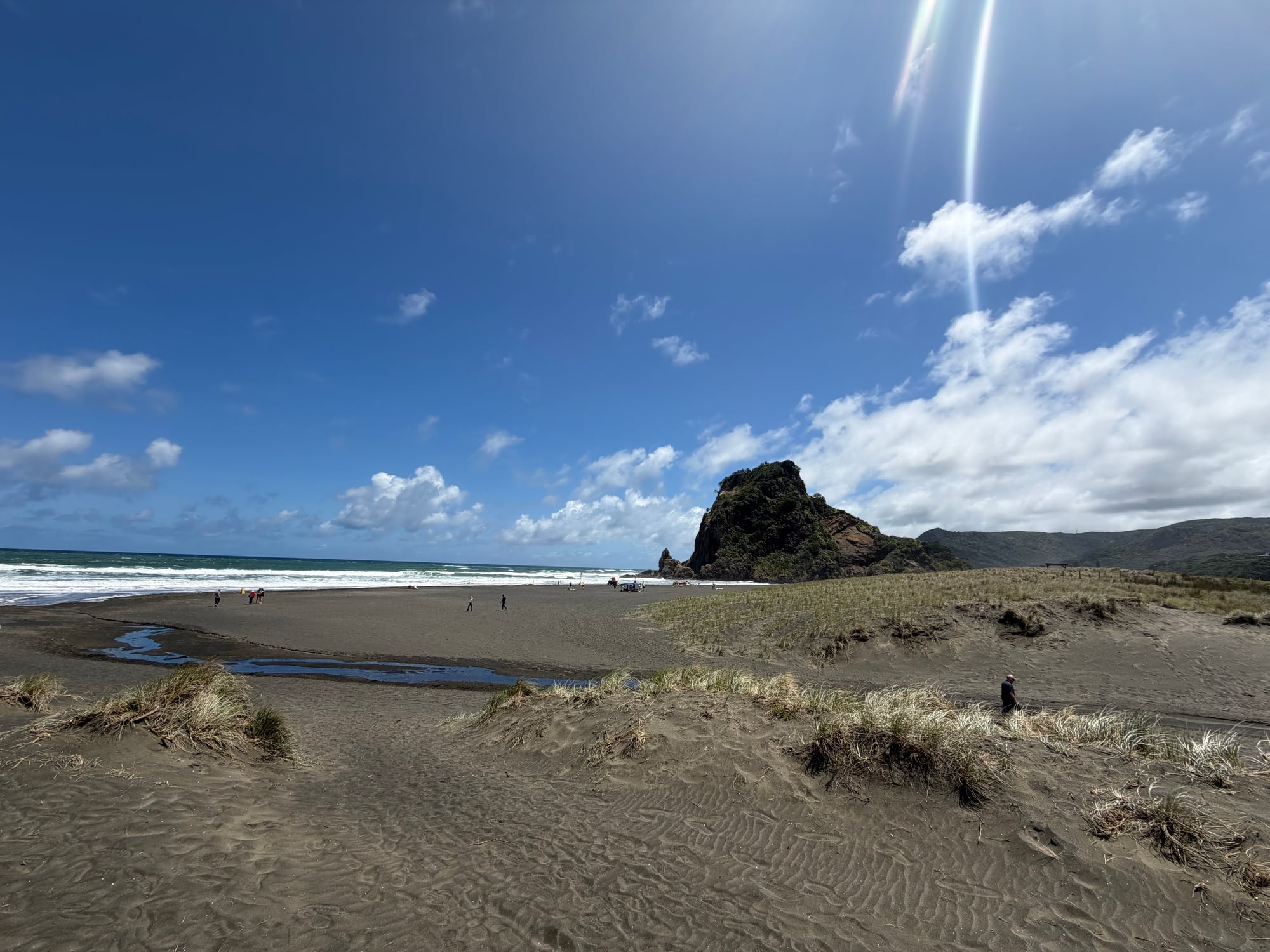 Wide view of Piha Beach with dark sand, ocean, and rocky outcrop.