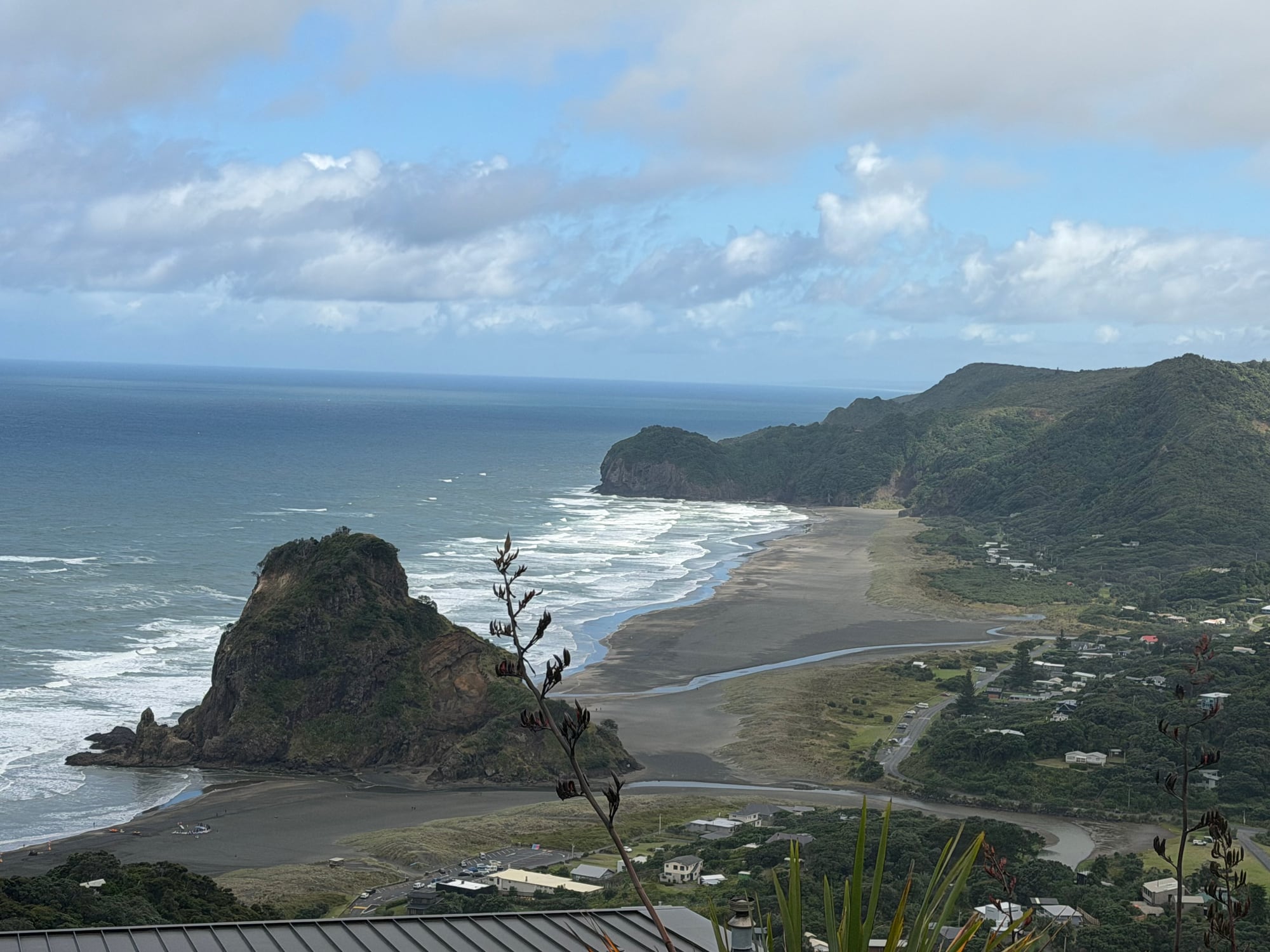 Elevated view of Piha Beach, coastline, and surrounding green hills.