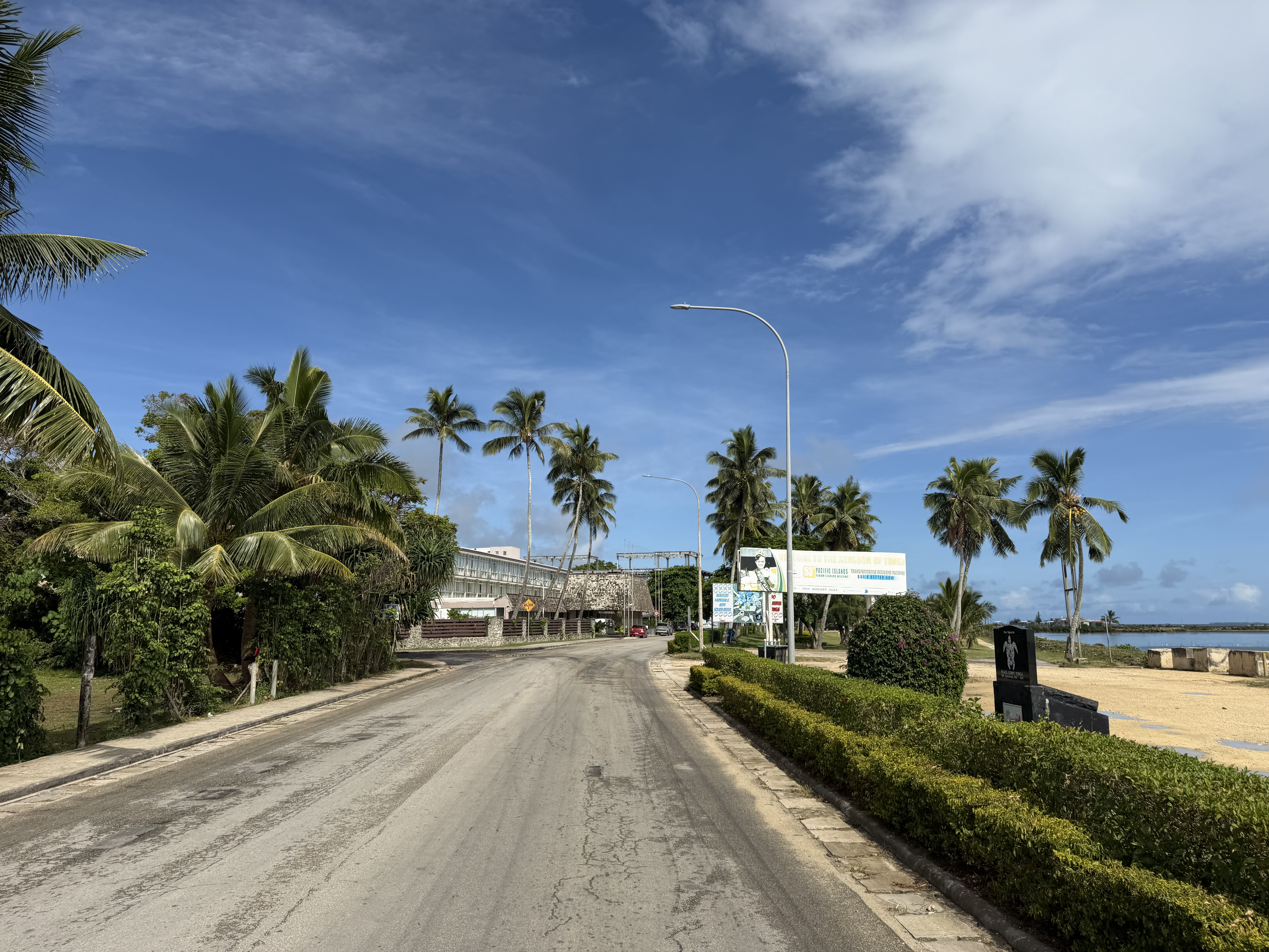 A palm-lined waterfront road beneath a wide blue sky in Tonga.