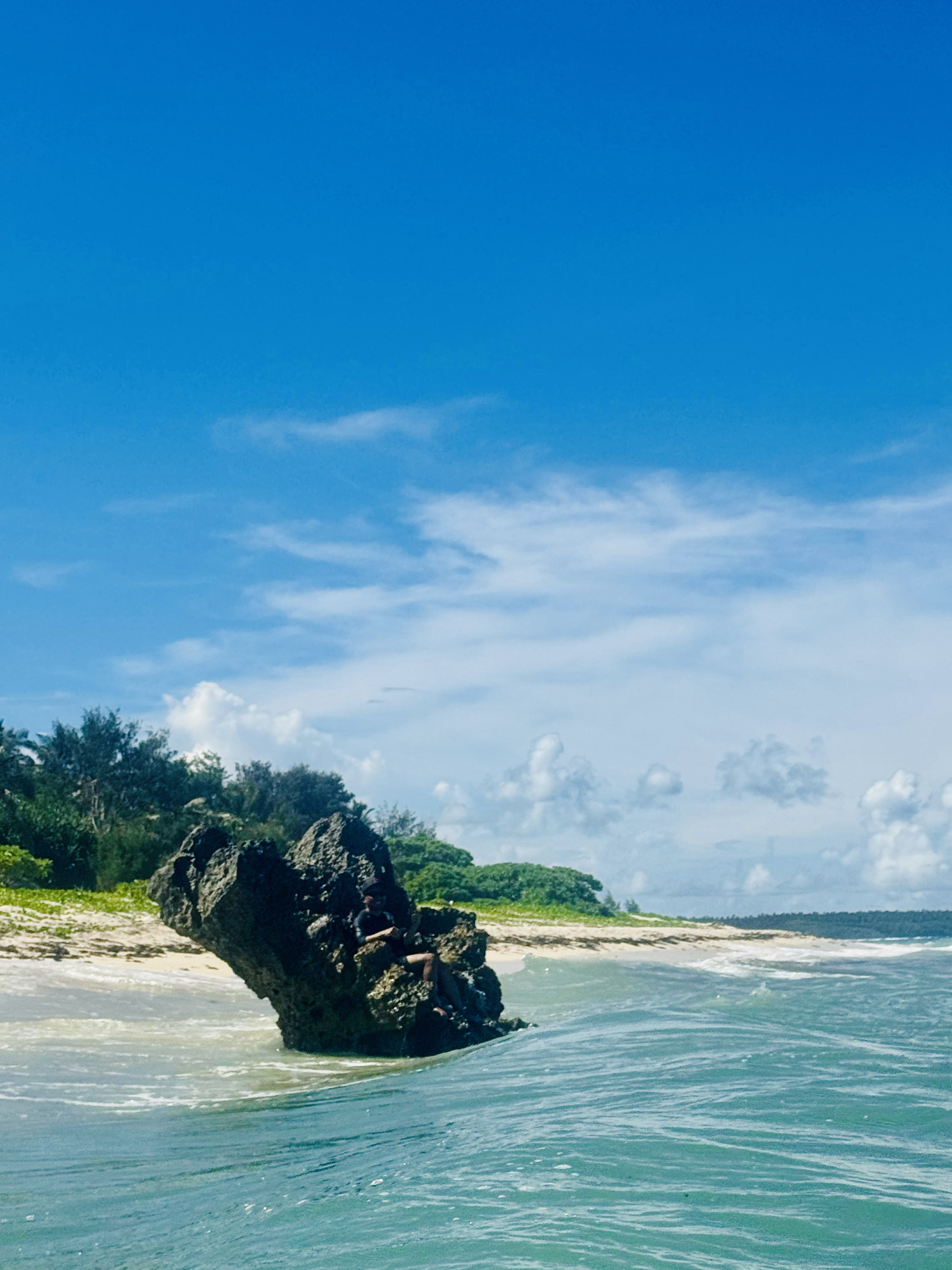 A person sitting on a large coastal rock surrounded by turquoise water in Tonga.