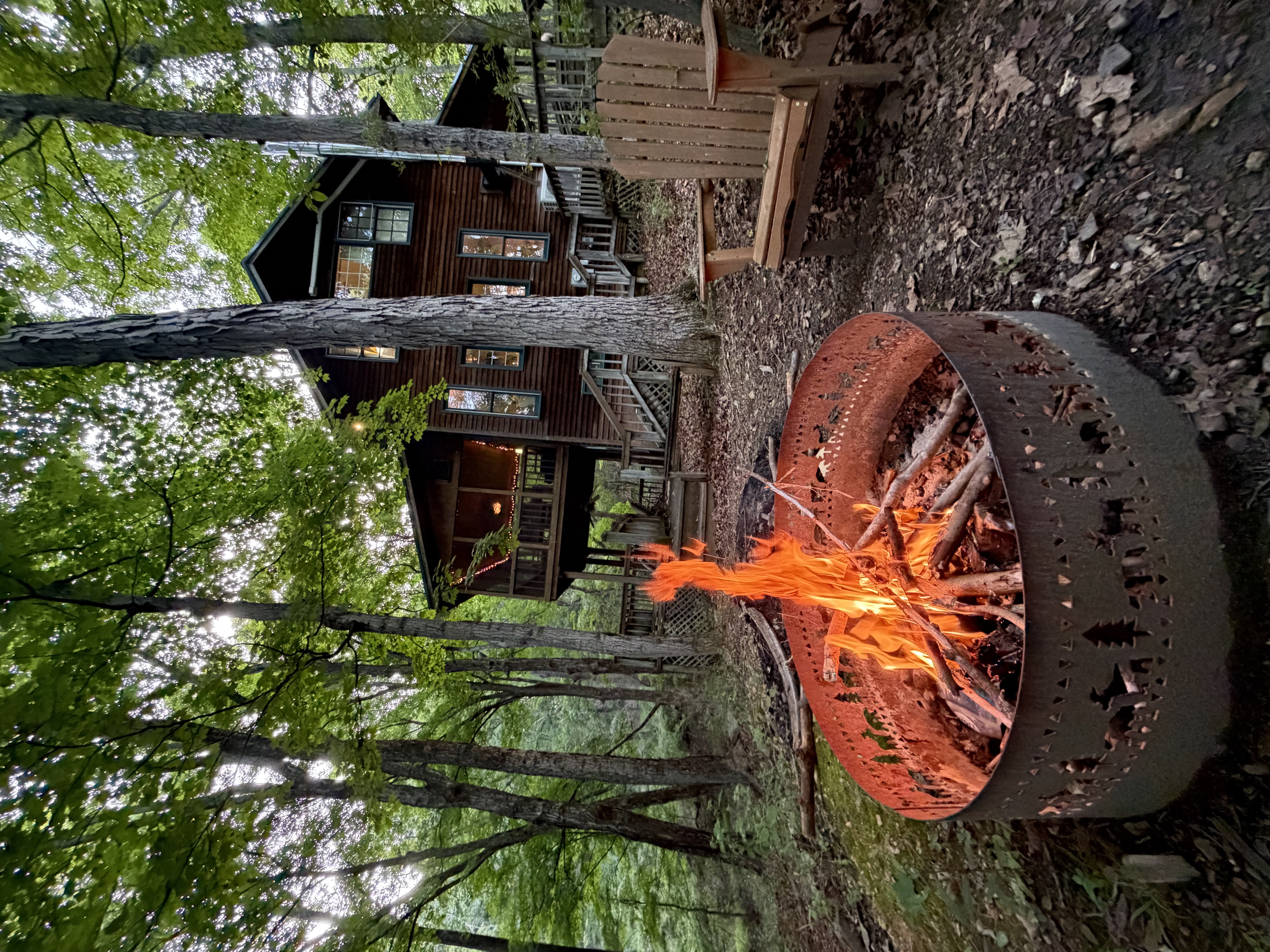 A campfire burning beside a wooden cabin in the forest.