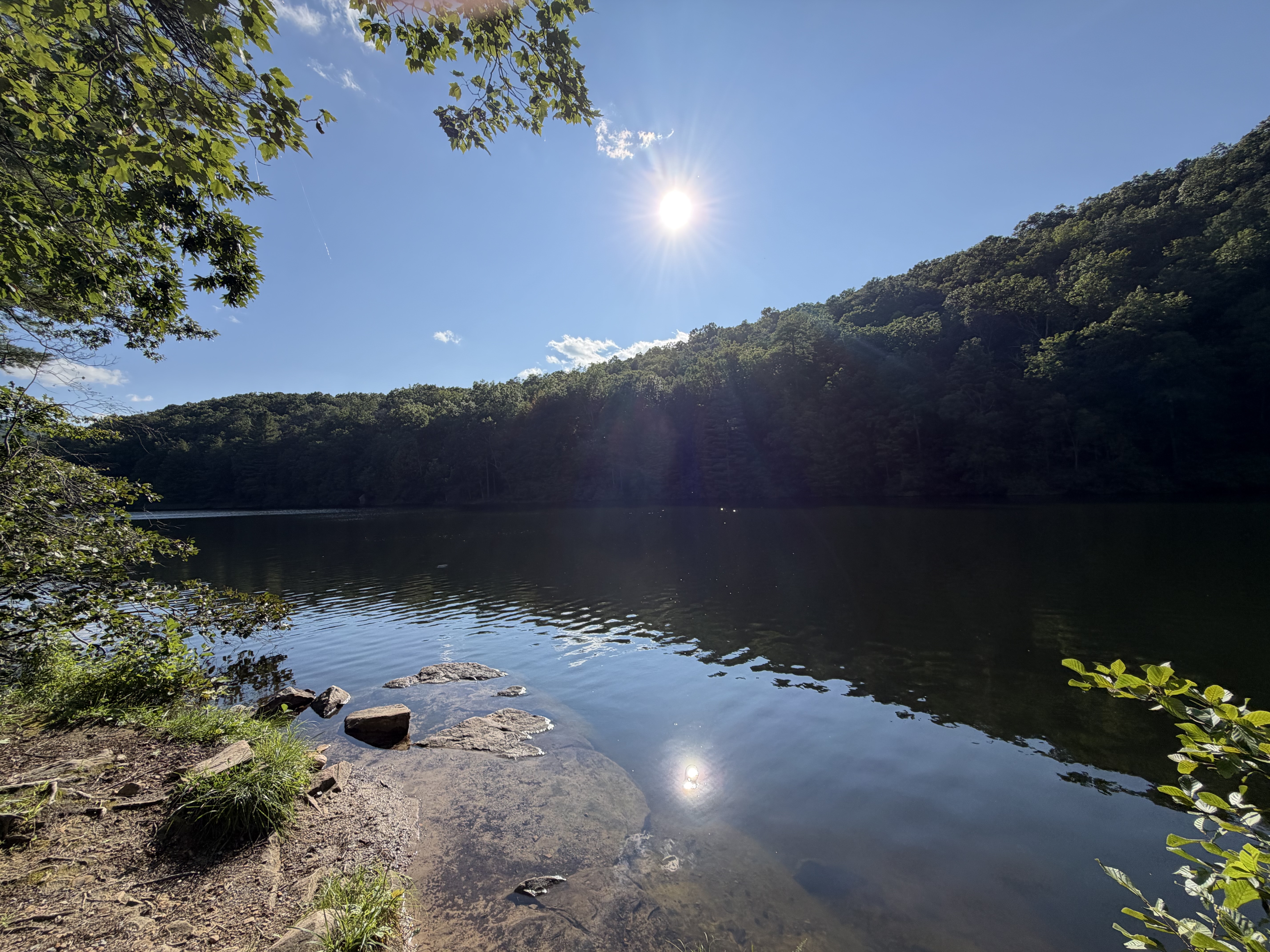 Sunlight reflecting across a quiet mountain lake surrounded by forest.